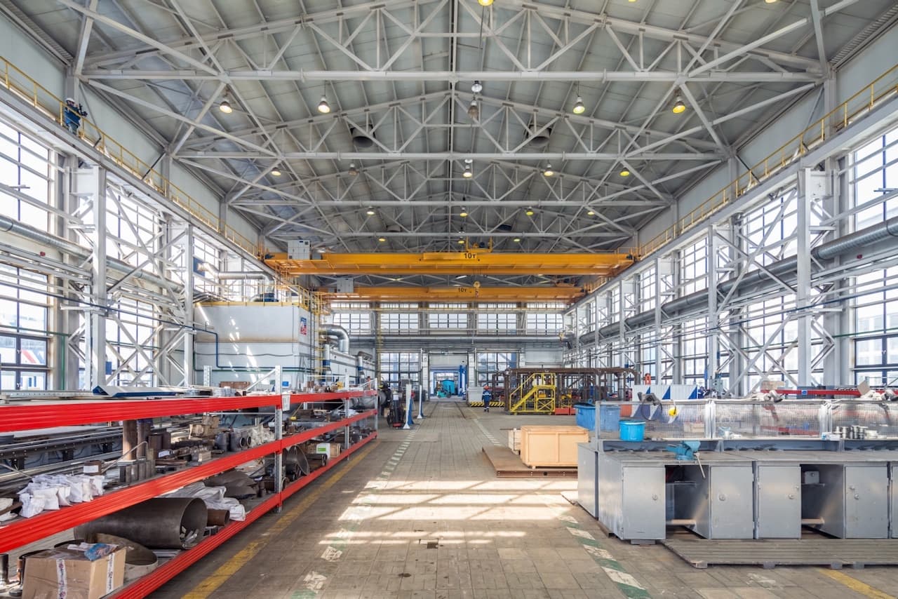 Espacio industrial amplio con maquinaria pesada y grúas, ventilado por Equipos de Aire Acondicionado Portátiles para mejorar el flujo de aire.