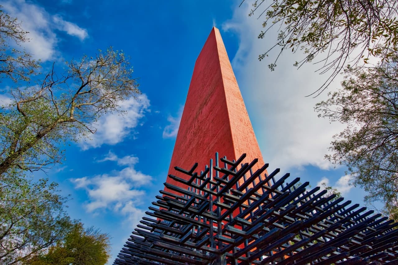 Escultura emblemática en un entorno urbano abierto, con un cielo azul brillante y el uso de Equipos de Aire Acondicionado Portátiles en áreas adyacentes.