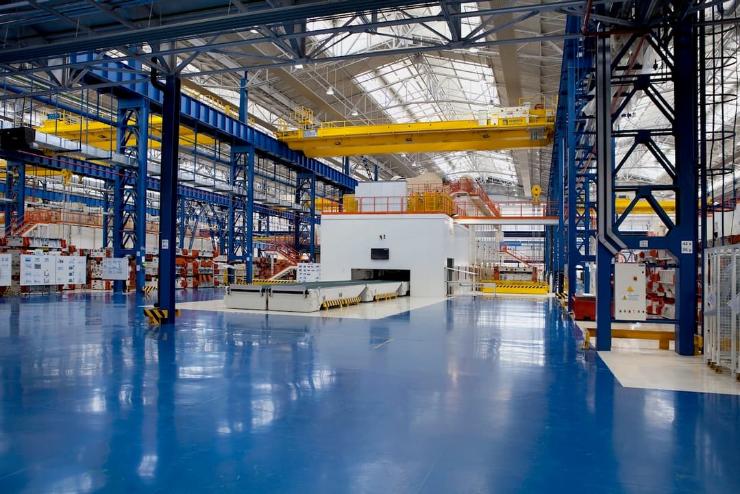 Interior de una fábrica moderna con techos altos y maquinaria pesada, ventilada por sistemas TBSI-580 para mantener el ambiente fresco.