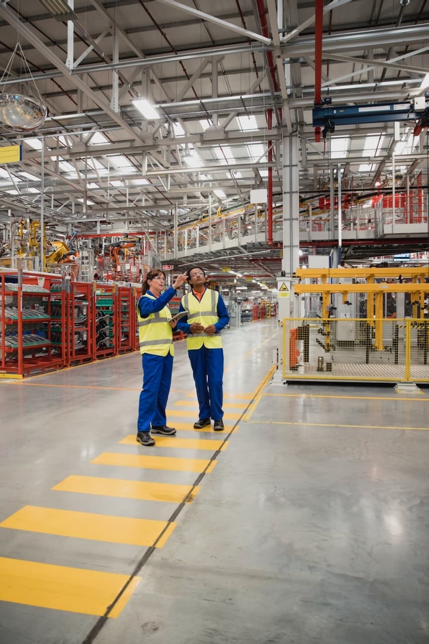 Dos trabajadores en una línea de ensamblaje industrial, con sistemas de ventilación TBSI-580 proporcionando aire limpio.